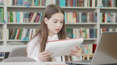 Uzun kahverengi saçlı odaklanmış bir genç kız renkli bir kütüphanede modern bir masada otururken elinde bir defter tutarak çalışmalarıyla derinden meşguldür. Kitaplarla dolu raflarla çevrili akademik adanmışlık ruhunu somutlaştırıyor.