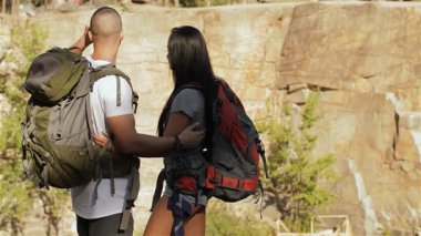 Bir çift genç yürüyüşçü yan yana duruyor, nefes kesici bir manzaraya dürbünle bakıyorlar. Sakallı beyaz adam dürbünü, hem açık hava kıyafetleriyle süslenmiş hem de macera ruhunu somutlaştıran çarpıcı esmer kız arkadaşına veriyor.