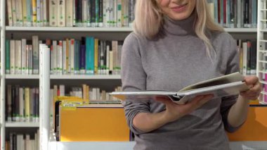 Sarı saçlı neşeli bir kadın, renkli kitaplıklarla dolu canlı bir kütüphanede sayfalarını zevkle çeviriyor. Bu sahne öğrenmenin ve hayal gücünün özünü yansıtıyor, eğitimin güzelliğini ve neşesini gösteriyor.