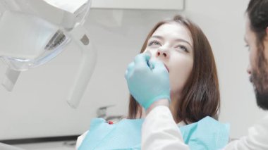 Neşeli genç bir kadın kameraya parlak bir gülümseme gösterir, diş muayenesinden sonra mutluluk saçar. Modern klinikteki neşeli atmosfer, aldığı profesyonel bakımdan duyduğu güven ve memnuniyeti vurguluyor.