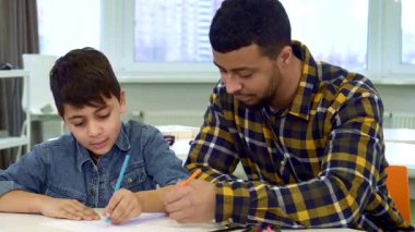 Çekici bir baba ve küçük esmer oğlu masada keyifli bir çizim seansına dalmış, gülücüklerini ve yaratıcılıklarını paylaşıyorlar. Genç Afrikalı Amerikalı çocuk heyecanla renkli yüzünü gösterirken dikkatle çocuğuyla meşgul oluyor.