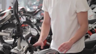 Çekici bir gülümsemesi olan genç beyaz bir adam parlak siyah bir motosiklete doğru eğiliyor ve benzin deposunu hayranlıkla okşuyor. Bu canlı sahne, güçlü bir motosiklet satın almanın heyecanını yakalıyor. Heyecan, hız ve tutkuyu gözler önüne seriyor.