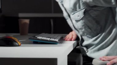 Kesilmiş bir atış, bir adamı güvenli bir şekilde sandalyesine oturturken yakalar, bilgisayarına bağlanmaya hazırlanır. Eli masanın üzerinde duruyor, daktilo etmeye hazır, üretkenlik ruhunu somutlaştırıyor ve modern çalışma alanında azim gösteriyor.