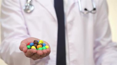 Gıcır gıcır beyaz önlüklü şefkatli bir erkek doktor elinde renkli bir tatlı çeşidi ve hoşgörü ile sağlıklı seçimler arasındaki dengeyi sembolize eden parlak bir elma tutuyor. Yumuşak beyaz bir arkaplanda geçen bu canlı sahne,
