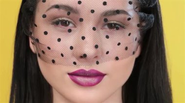 Bu çarpıcı yakın plan, zarif siyah duvağı, parlak erik dudakları ve büyüleyici gözleriyle seyirciyi büyüleyen güzel bir Asyalı mankeni gösteriyor. Parlak sarı bir arkaplan üzerine kurulmuş görüntü zarafet ve şehvet yayıyor.