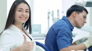 Parlak bir diş kliniğinde, odaklanmış bir diş hekimi hastaya ustalıkla dişlerini dökerken, neşeli bir bayan asistan da baş parmak hareketi yapıyor. Bu canlı sahne, diş bakımındaki takım çalışmasını ve pozitifliği yakalıyor.