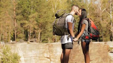 Canlı sırt çantaları olan bir çift genç yürüyüşçü, yemyeşil yeşilliklerle çevrili, çarpıcı bir uçurumun kenarında şefkatli bir öpücük paylaşıyor. Neşeli ifadeleri ve geniş kanyon görüşleri doğada mükemmel bir aşk ve macera anı yaratır.
