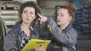 Birinde kıvırcık saçlı, diğerinde parlak kırmızı bukleli iki kadın mühendis, yoğun bir metal deposundaki belgeleri incelerken hararetli bir tartışmaya giriştiler. Takım çalışmaları, güçlenmeyi ve profesyonelliği temsil etmektedir.