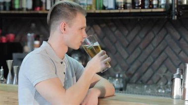 Şık sarı saçlı, neşeli beyaz bir adam, bir bardak soğuk bira kaldırıyor, gösterişli bar tezgahına yaslanıyor. Sıcak gülüşü ve rahat duruşu davetkar bir atmosfer yaratıyor. Arkadaşlarıyla eğlenmek için mükemmel bir ortam.