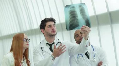 Zarif, iyi ışıklandırılmış bir hastane ortamında üç kendine güvenen doktor ve bir kadın sağlıklı akciğerlerin röntgenini dikkatle inceliyor. Odaklanmış ifadeleri ve profesyonel kıyafetleri hasta bakımına olan bağlılıklarını ve önemini vurguluyor.