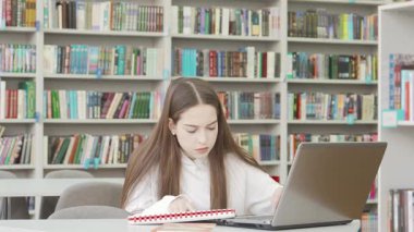 Genç bir kız kütüphane masasında oturuyor, dizüstü bilgisayarında projesiyle boğuşurken gözle görülür bir şekilde bunalmış. Renkli kitaplarla çevrelenmiş, çatık kaşları ve gergin duruşu, yaklaşan teslim tarihleri ve akademik kaygıların baskısını yansıtıyor.