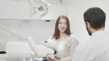 Neşeli bir kadın, diş muayenesinden sonra aynada ışıldayan gülüşüne hayran oluyor. Parlak, modern klinik ayarları onun neşeli davranışlarını geliştiriyor, diş tedavisinin başarısını ve aldığı tedaviyi yansıtıyor.