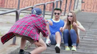 Neşeli bir üçlü dışarıda keyifli bir anın tadını çıkarıyor. Bir arkadaş, basamaklarda poz verirken diğer ikisinin fotoğrafını çekiyor. Kahkahaları ve enerjik enerjileri, dostluğun ve kaygısızlığın özünü gösteren canlı bir atmosfer yaratıyor.