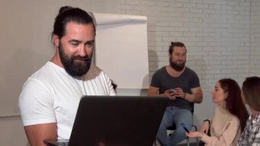 Olgun sakallı bir iş adamı dizüstü bilgisayarına özenle yazı yazarak enerjik iş adamları arkasında tartışırken kendine güveniyor. Bu hareketli ofis sahnesi takım çalışmasının ve işbirliğinin özünü yakalar.