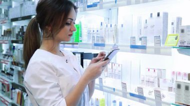 Odaklanmış genç bir kadın eczacı, iyi organize edilmiş bir eczane rafından ilaç seçerken dijital tablet üzerinde ustaca yol alır. Bu canlı sahne onun profesyonelliğini ve olağanüstü bir sağlık hizmeti sunma isteğini yansıtıyor.