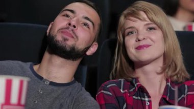 Neşeli genç bir çift, sinemadaki film karşısında büyülenmiş, samimi bir sinemada yan yana oturur. Ellerindeki patlamış mısırla ve yüzlerindeki gülümsemeyle, ortak deneyimlerin ve sinematik maceraların neşesini somutlaştırıyorlar.