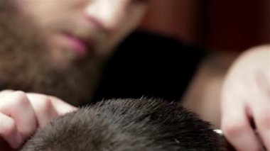Hareketli bir berber dükkanında, yetenekli bir berber titizlikle kurutur ve bakımlı sakallı, modaya uygun bir gencin saçını şekillendirir. Atmosfer canlı ve şık, erkeklerin tımar sanatını ve berber ile müşteri arasındaki bağı gösteriyor.
