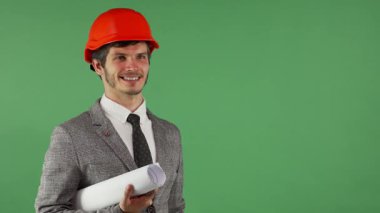 Şık bir takım elbise içinde neşeli bir genç adam ve parlak turuncu parlak turuncu şapka ışınları elinde yuvarlak bir plan ve davetkar bir şekilde el kol hareketi tutarken. Parlak yeşil renkli bir arkaplan üzerine kurulmuş bu görüntü pozitiflik ve profesyonellik yayar.