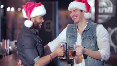 İki neşeli Noel Baba kılıklı arkadaş canlı bir barda buzlu bira bardaklarını kaldırarak mutluluk ve dostluk saçıyorlar. Bayram ruhunu kutlarken neşeli atmosfer heyecan vericidir. Etrafı kahkahalarla ve eğlenen arkadaşlarla çevrilidir.