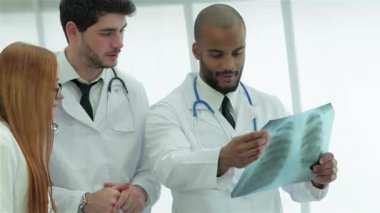 Dört kendinden emin doktor, iki erkek ve iki kadından oluşan çeşitli bir ekip, sigara içmenin tehlikelerini vurgulayarak sağlıklı akciğerlerin röntgenini yakından inceliyor. Mesleki kıyafetleri ve odaklanmış ifadeleri sağlık eğitimine olan bağlılıklarını yansıtıyor.