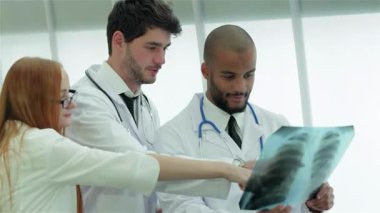 Üç kendine güvenen doktor, bir erkek ve bir kadın, sigara içmenin tehlikelerini tartışırken sağlıklı akciğerlerin röntgenini incelerken odaklanmış bir konsültasyona giriyorlar. Profesyonel kıyafetleri ve özenli ifadeleri takım çalışmasını ve bağlılığını vurguluyor