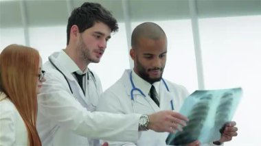 Parlak, modern bir klinikte, üç kendine güvenen doktor ve bir kadın, uzmanlıklarını ve takım çalışmalarını gösteren sağlıklı akciğerlerin röntgenini analiz ederler. Sahne, doktorların çıtır çıtır giyindiği profesyonellik ve hasta bakımına adanmışlık yayıyor.