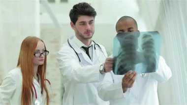 Parlak, modern bir klinikte, üç kendine güvenen doktor ve bir kadın, uzmanlıklarını göstermek için sağlıklı akciğerlerin röntgenini çekiyorlar. Odaklanmış ifadeleri ve profesyonel kıyafetleri, sağlık sektöründe takım çalışmasının önemini vurguluyor.