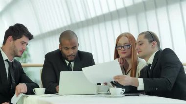 Dört gülümseyen iş adamından oluşan dinamik bir grup, şık ofis dekoru ve parlak doğal ışık ile çevrili bir işbirliği toplantısına girişiyor. Özgüvenli ifadeleri ve odaklı tartışmaları, belgeleri incelerken takım çalışmasının ve başarının altını çiziyor.