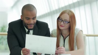 Odaklanmış bir işadamı ve kendine güvenen bir iş kadını, şık ve çağdaş bir ofis alanında önemli belgeleri birlikte gözden geçiriyorlar. Gülüşleri ve özenli ifadeleri verimli bir atmosferi yansıtıyor.