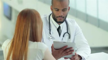 Gıcır gıcır beyaz önlük ve steteskop giyen kendini işine adamış bir doktor, sıcak ve profesyonel bir atmosfer sergileyen bir hastayla sağlık sorunlarını dikkatlice tartışıyor. Bu etkileşim, sağlık hizmetlerinde iletişimin önemini vurguluyor.