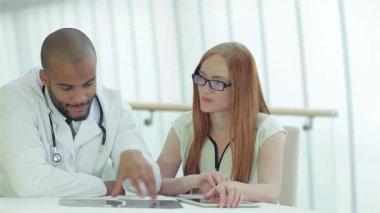 Kendini işine adamış beyaz önlüklü bir doktor göğüs röntgenini incelerken bir hastayla düşünceli bir konuşma yapar. Parlak, modern klinik kurulumu güven ve profesyonellik atmosferini artırarak, önemini vurguluyor