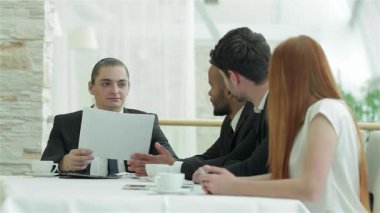 Kendine güvenen bir işadamı, parlak ve modern ofis ortamında meslektaşlarının dikkatini çeken bir belge tutuyor. Atmosfer, dört başarılı profesyonelin dinamik bir tartışmaya girmesi ve takım çalışması sergilemesi beklentisiyle dolu.