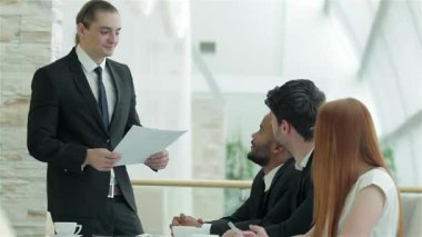 Karizmatik bir işadamı, parlak ve modern bir ofiste nişanlı meslektaşlarına önemli belgeler dağıtıyor. Atmosfer, resmi giyinmiş dört profesyonel olarak işbirliği ve başarı ile suçlanıyor.