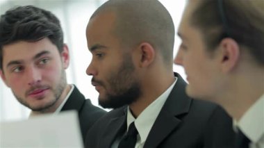 Sivri takım elbiseli üç kendine güvenen işadamı şık bir ofis masasında başarı ve dostluk saçan stratejileri tartışıyorlar. İfadeleri coşku ve kararlılığı yansıtıyor, ilham verici bir atmosfer yaratıyor.