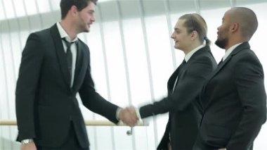 Sivri takım elbiseli iki kendine güvenen işadamı, sıkı bir tokalaşma içindeler, modern ofis ortamında başarı ve dostluk yayıyorlar. Gülüşleri umut verici bir ortaklığı yansıtıyor. Parlak, havadar bir atmosferle çevrili.