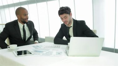 Kendine güvenen iki genç iş adamı, çizelgeler ve bir dizüstü bilgisayarla çevrili şık bir masada canlı bir sohbete girişiyor. Gülüşleri pozitiflik ve işbirliği saçıyor, çağdaş bir şirkette takım çalışması ve yenilik ruhunu somutlaştırıyor.