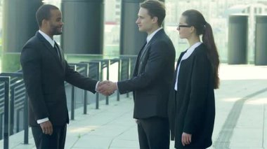 Zarif resmi kıyafetler içindeki güler yüzlü iş adamlarından oluşan dinamik bir üçlü, başarılı bir ortaklığı simgeleyen sıcak bir tokalaşmaya giriyorlar. Modern bir kentsel zemin üzerine kurulmuş bu sahne pozitiflik ve işbirliği yayıyor,