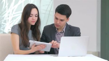 Genç, çekici bir iş adamı ve kadın, her ikisi de kameraya içten bir şekilde gülümseyen gösterişli bir tablet üzerindeki verileri analiz ederken canlı bir tartışmaya girişirler. Modern ofis dekorları, bir dizüstü bilgisayar ve parlak, havadar bir atmosferle birlikte, duyularını geliştirir.