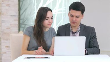 Genç, çekici bir iş adamı ve kadın, gösterişli bir dizüstü bilgisayarda gösterilen verileri karşılaştırarak derin bir tartışmaya girişiyor. Kadın bu modern ofis ortamında işbirlikçi bir ruh sergileyerek onaylıyor.
