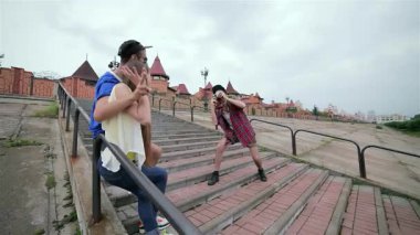 Üç genç arkadaş neşe ve kahkaha paylaşıyor ve neşeli bir poz veriyorlar. Canlı açık hava basamaklarında, kaygısız ruhlarını sergiliyorlar. Sahne mutluluk saçıyor, neşeli jestler ve parlak gülücüklerle, arkadaşlığın özünü somutlaştırıyor ve