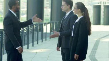 Şık giyinmiş güler yüzlü iş adamlarından oluşan canlı bir grup kalabalık bir şehir caddesinde yeni ortakları selamlıyor. Coşkulu tokalaşmaları ve dostça ifadeleri yeni bir heyecanın göstergesi olarak davetkar bir atmosfer yaratıyor.