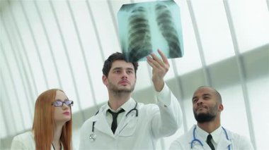 Üç kendine güvenen doktor, bir erkek ve iki kadın, sigara içmenin tehlikelerini vurgulayarak sağlıklı akciğerlerin röntgenini dikkatle inceliyorlar. Profesyonel kıyafetleri ve odaklanmış ifadeleri bir uzmanlık ve sağlığa adanmışlık ortamı yaratıyor.