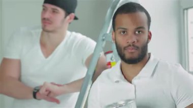 Parlak, boş bir dairede, kararlı genç bir işçi bir boya kutusunu kavrıyor, arkaplandaki merdivenin üzerinde güvenle dururken, yeri değiştirmeye hazır. Bu dinamik ikili, nefes almaya hazırlanan takım çalışmasını ve yaratıcılığını somutlaştırıyor.