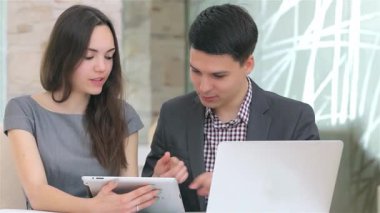 Genç, şık bir iş adamı ve kadın, modern ofis ortamındaki şık bir tabletteki verileri analiz ederek derin bir tartışmaya girişiyor. Odaklanmış ifadeleri ve işbirlikçi ruhları takım çalışmasının ve yeniliğin özünü canlı bir şekilde vurgular.