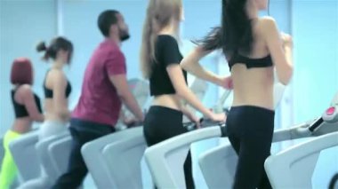 Erkekler ve kadınlar da dahil olmak üzere çeşitli atletler koşu bantlarında enerjik bir şekilde koşuyor ve spora olan bağlılıklarını sergiliyorlar. Sahne, renkli spor kıyafetleri ve odaklanmış ifadelerle antrenmanlarının yoğunluğunu yakalıyor.