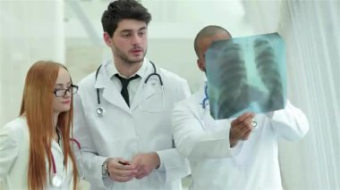 Üç kendine güvenen doktor, bir erkek ve iki kadın, sigara içmenin tehlikelerini vurgulayarak sağlıklı akciğerlerin röntgenini dikkatle inceliyorlar. Profesyonel kıyafetleri ve odaklanmış ifadeleri, sağlık sektöründe takım çalışmasının güçlü bir imajını yaratıyor.