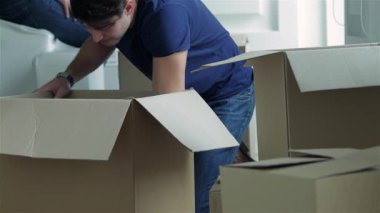 Parlak, boş bir dairede, sevgi dolu bir çift, kocanın arkasından şakacı bir şekilde kocasını kucakladığı kutuları açıyor. Gülümsemeleri, yeni evlerine taşınmanın heyecanını kucaklarken mutluluk saçıyor.
