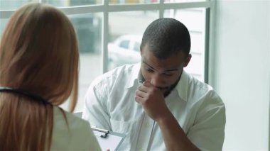 Parlak ve modern bir klinikte, odaklanmış bir hasta, doktorunun değerli tıbbi tavsiyelerini dikkatle dinler. İlgili doktor, boynunda steteskopla hastanın anlaşılmasını ve desteklenmesini sağlarken bir reçete yazar.