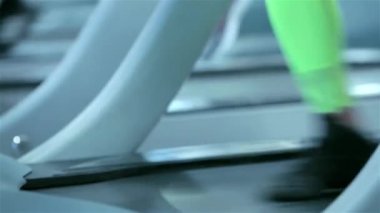 İnce, parlak siyah taytlar içinde atletik bacaklar, koşu bandına ritmik bir şekilde vuruşlar, azim ve güç gösterisi. Canlı pembe ayakkabı bağcıkları şık spor salonuna doğru patlıyor. Enerjiyi ve odağı vurguluyor.