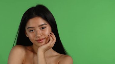 Uzun saçlı güzel bir Asyalı kadının büyüleyici portresi, neşeli bir ifadeyle neşe içinde gülümseyen, canlı yeşil bir krom anahtara dayanan. Kendine güveni ve ışıl ışıl gülüşü pozitifliğini ve çekiciliğini sergiliyor.